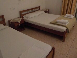 A hotel room with two single beds, wooden headboards, bedside tables, and a large window with curtains. - Estelle (Polygyros)