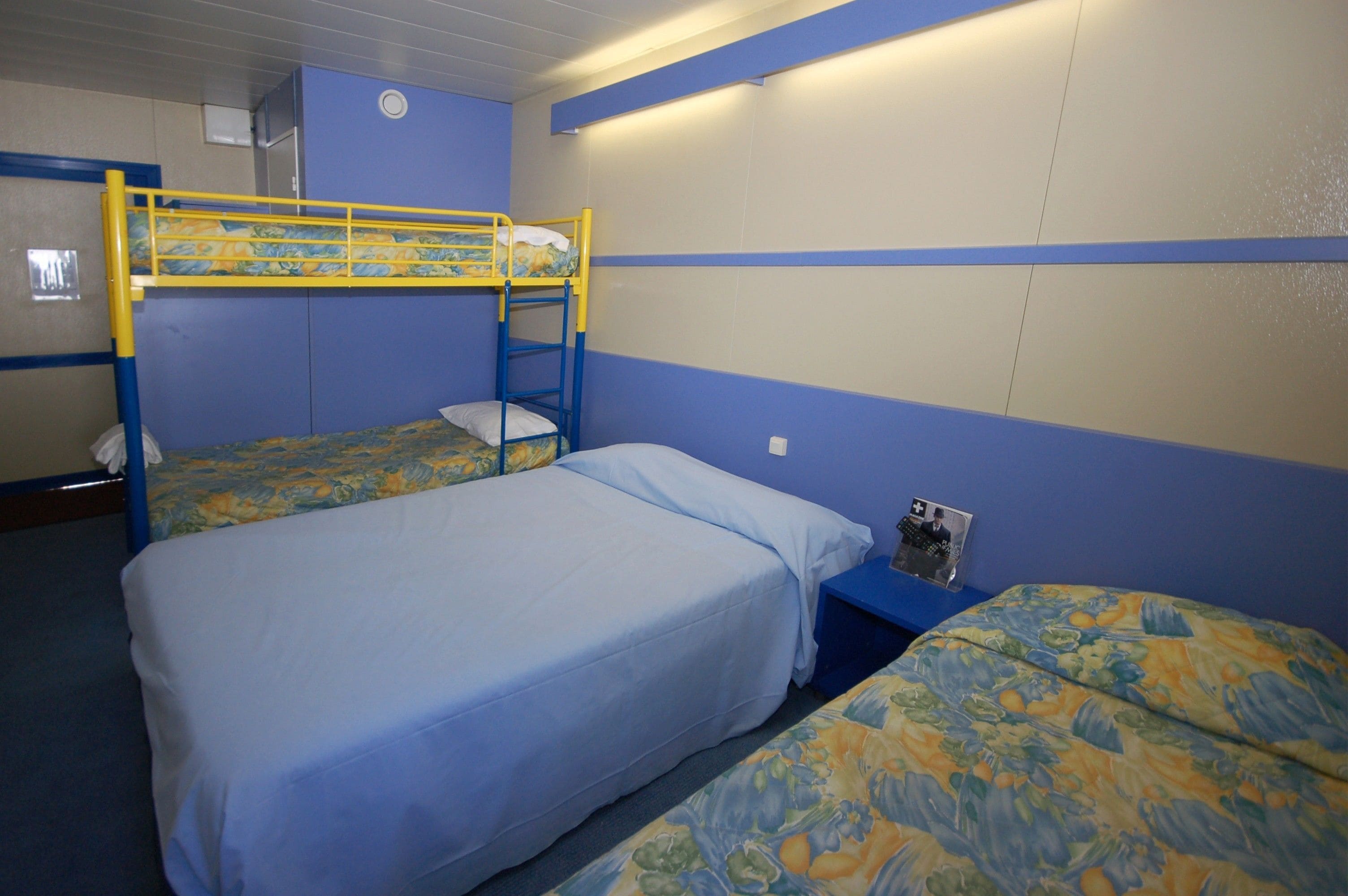 A bunk bed room with blue walls and a bunk bed with a yellow frame. There is a small table with a magazine on it.