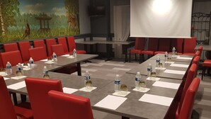 Un salón de conferencias con sillas y mesas rojas, equipado con botellas de agua y vasos.