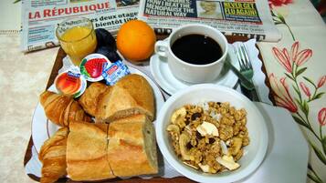 A breakfast tray with croissants, a bowl of granola, a glass of orange juice, and a cup of coffee, placed on a table with newspapers.