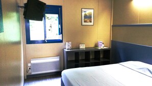 Habitación de hotel con cama, ventana, estante con objetos y televisor en la pared.