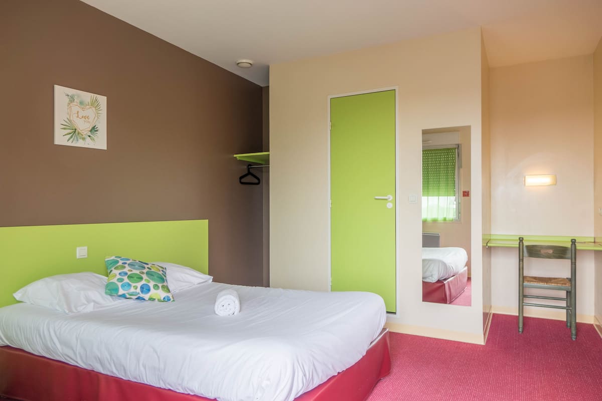 Habitación de hotel con una cama, una puerta verde, un escritorio pequeño y un espejo.