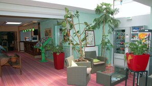 Un vestíbulo con muebles de mimbre, plantas en macetas, una máquina expendedora y una zona de recepción.