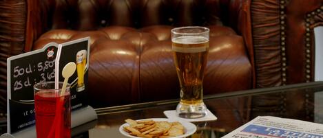 A leather sofa, a glass of beer, a plate of snacks, a menu, and a red drink on a table.