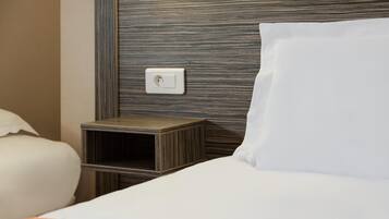 A hotel room with a neatly made bed, a small wooden nightstand, and a wall socket.