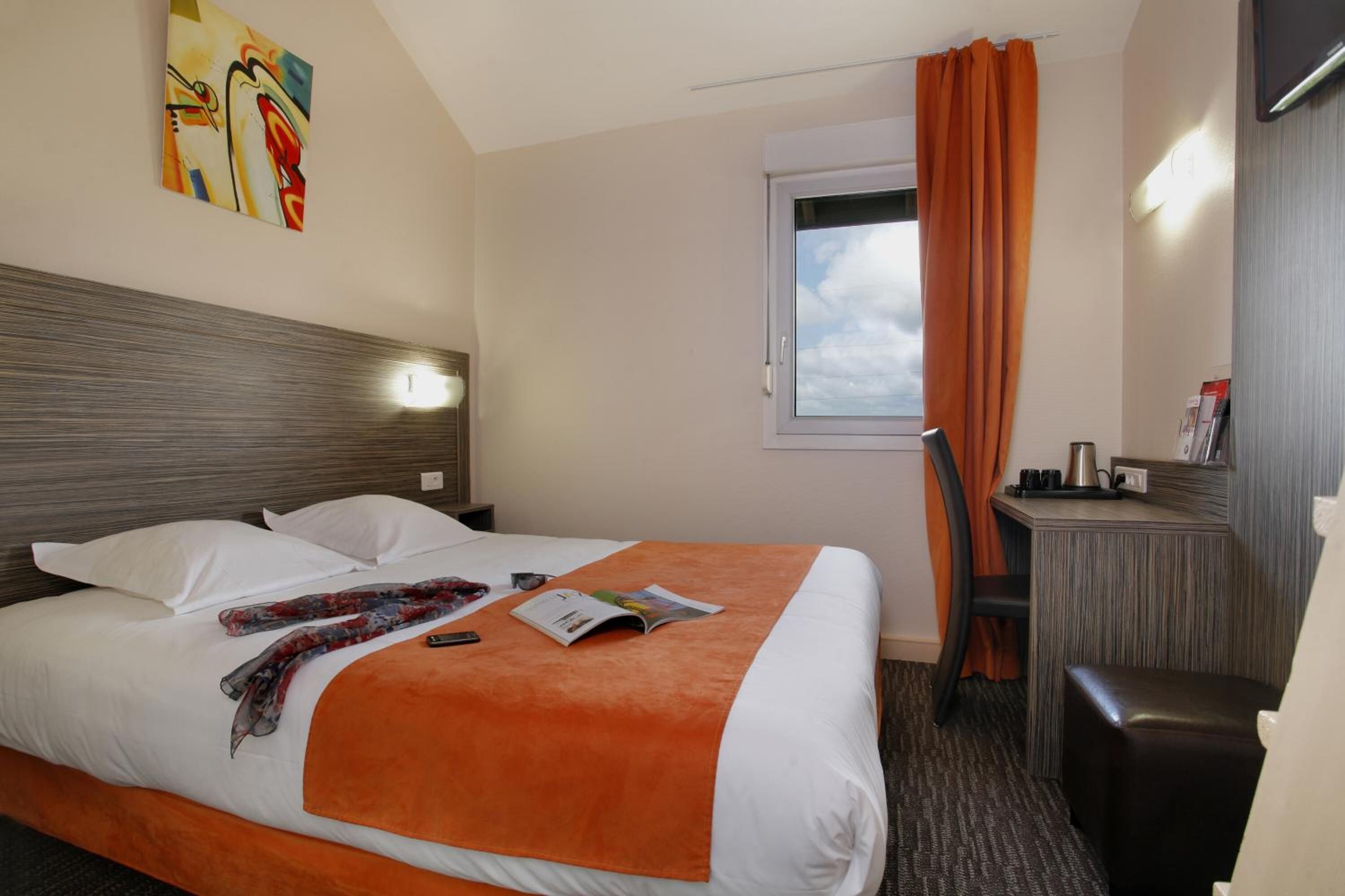 A hotel room with a bed, a desk, and a window with curtains.