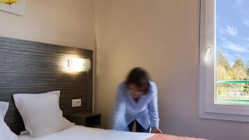 A hotel room with a bed, a nightstand, a wall-mounted light, and a window with a view of trees.