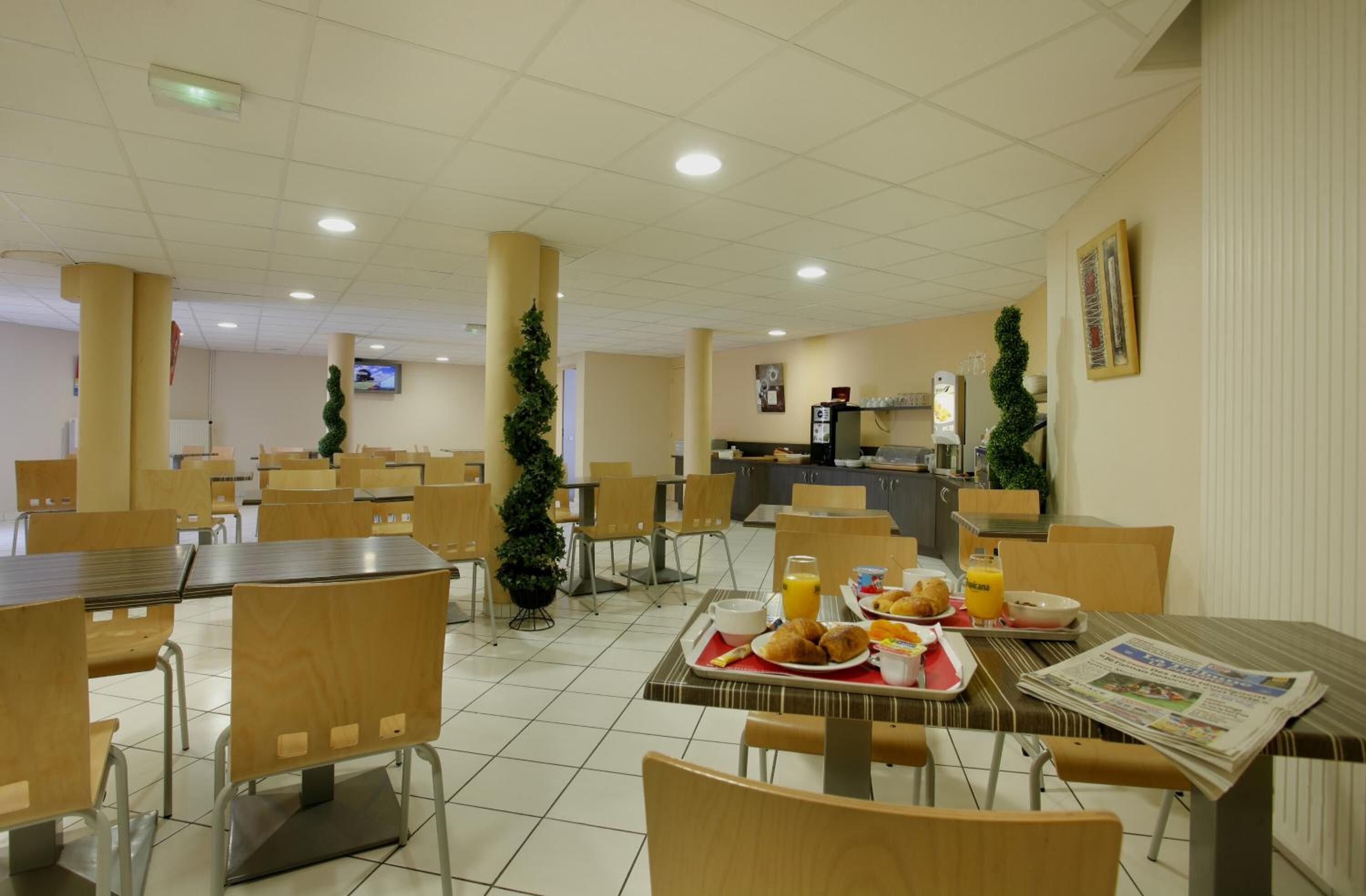 A cafeteria with tables and chairs, a refrigerator, and a television on the wall.