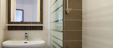 A bathroom with a white sink, a mirror, and a shower area with a glass partition.