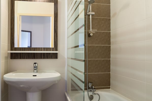 A bathroom with a white sink, a mirror, and a shower area with a glass partition.