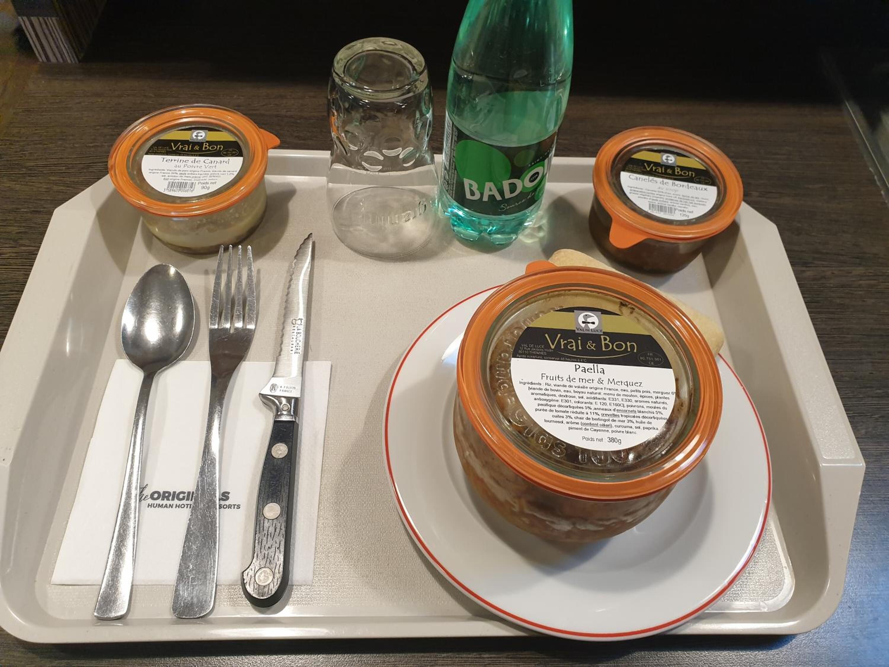 En bakke med ske, gaffel, kniv, to glas Vrai & Bon marmelade, et glas vand og en flaske Badoo.