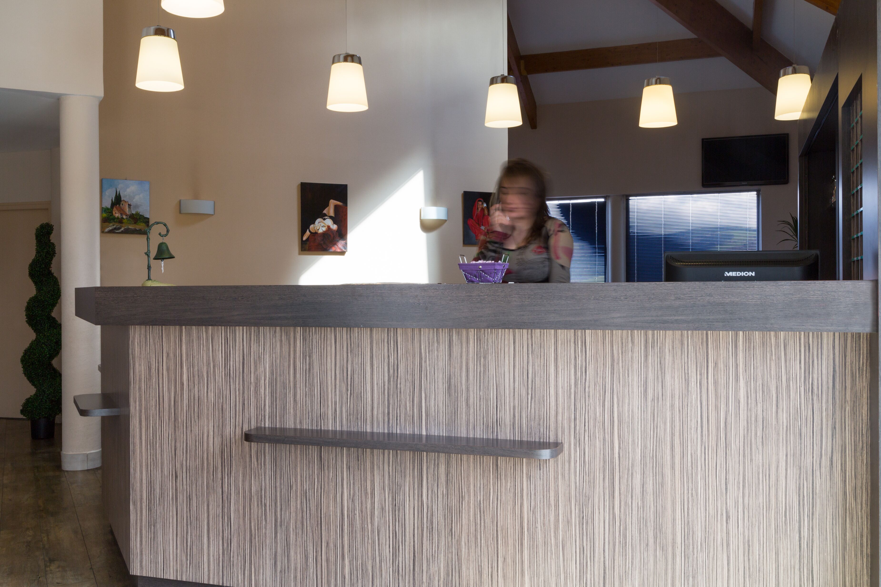 Een receptiebalie met een houten afwerking, hangende verlichting en een aan de muur bevestigde televisie.