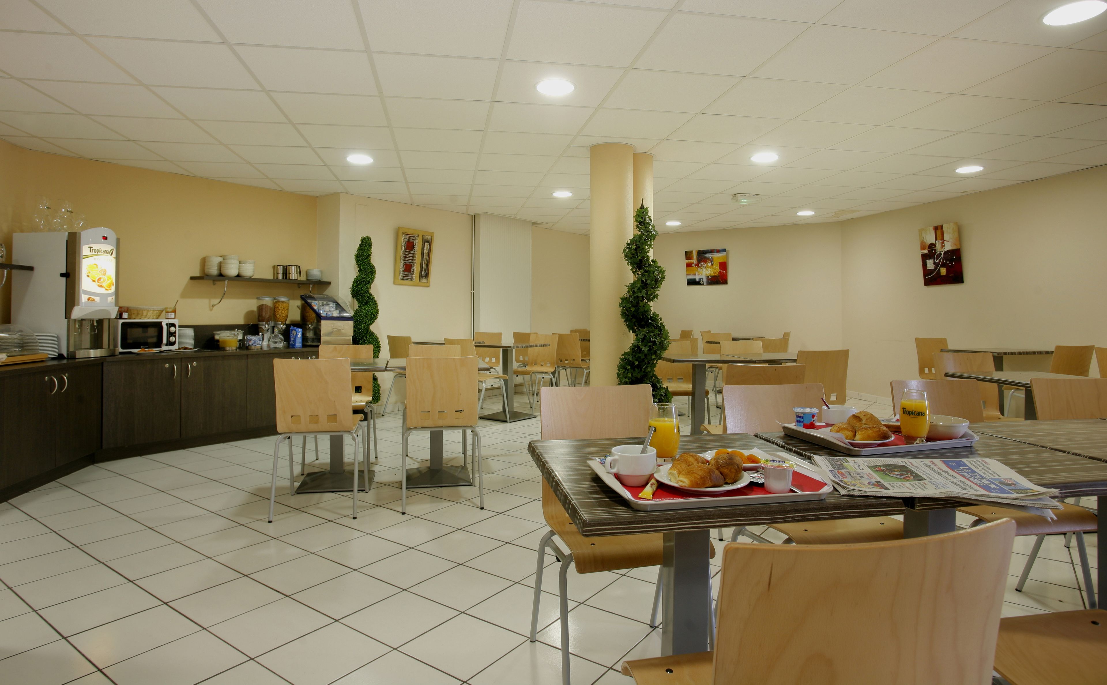 Eine Cafeteria mit mehreren Tischen und Stühlen, einer Kaffeemaschine und einer Theke mit Speisen.