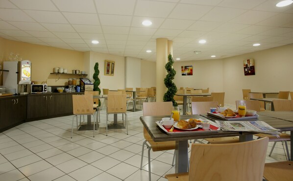 A cafeteria with multiple tables and chairs, a coffee machine, and a counter with food items.