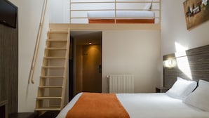 A hotel room with a bunk bed, a wooden ladder, a white bedspread, and a nightstand with a lamp.
