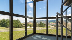 A room with large windows offering a view of a highway, greenery, and distant mountains.