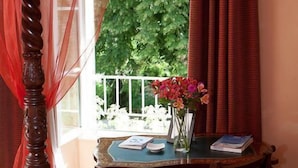 A room with a bed, a wooden chair, a table with a vase of flowers, and a window with curtains. - Logis Hôtel les Hauts de St Maure (Sainte-Maure-de-Touraine)