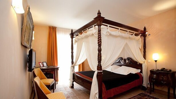A four-poster bed with a canopy, a chair, a bedside table, and a lamp. - Logis Hôtel les Hauts de St Maure (Sainte-Maure-de-Touraine)