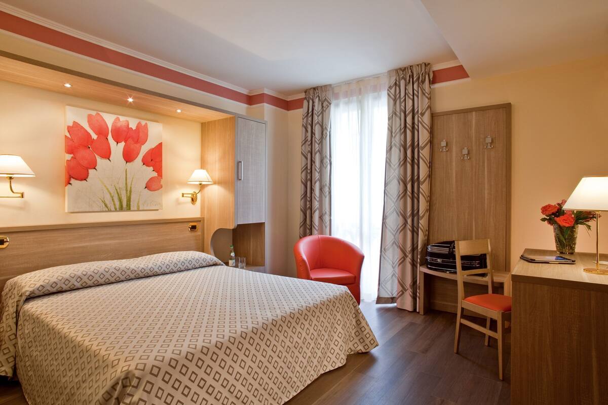 A hotel room with a bed, two chairs, a desk, and a wardrobe.