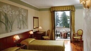 Quarto de hotel com duas camas, um quadro na parede, uma janela com cortinas e uma mesa com cadeiras do lado de fora.