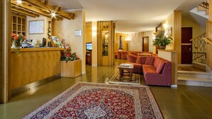 Um hall amplo com uma mesa de recepção de madeira, um tapete com padrão vermelho e uma escada.