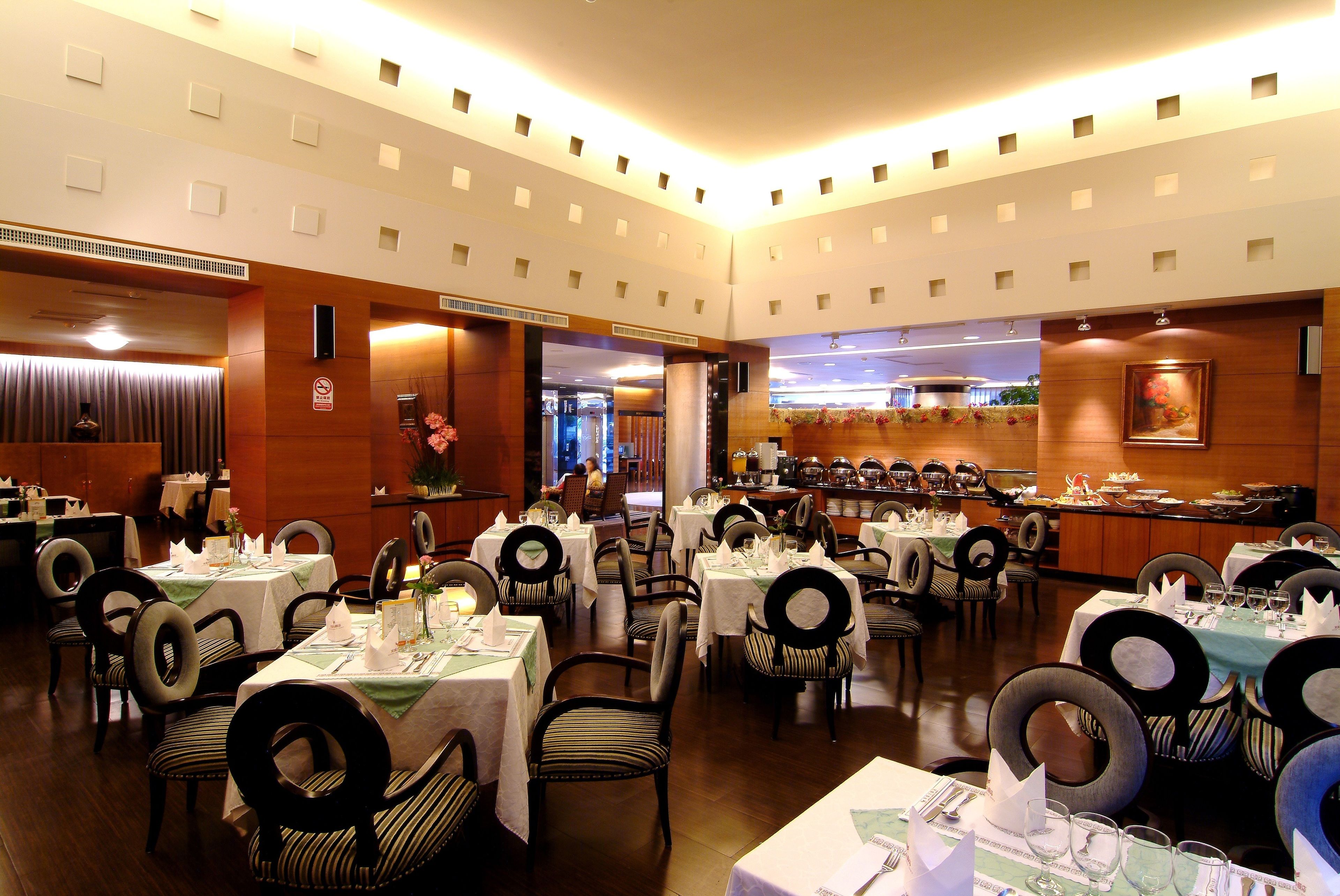 A hotel dining area with multiple tables set for guests, featuring a central bar and a view of the kitchen.