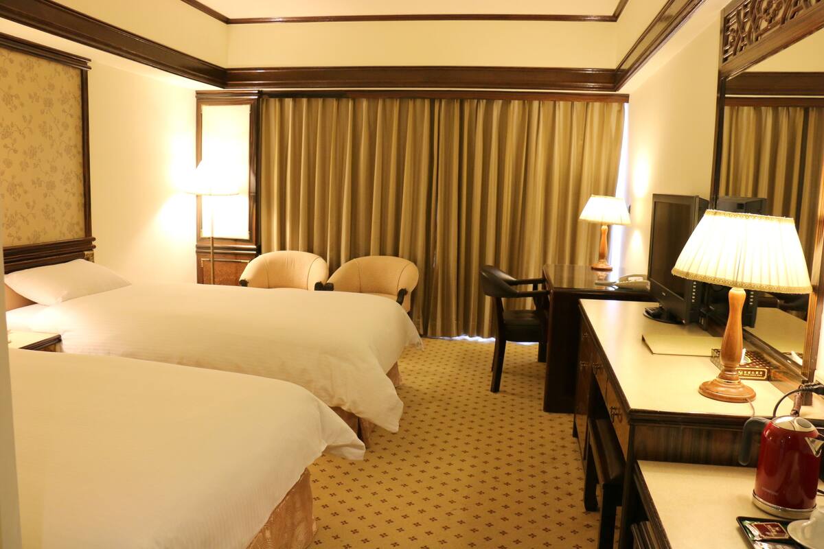 A hotel room with two beds, a desk, a chair, a television, and a mirror.