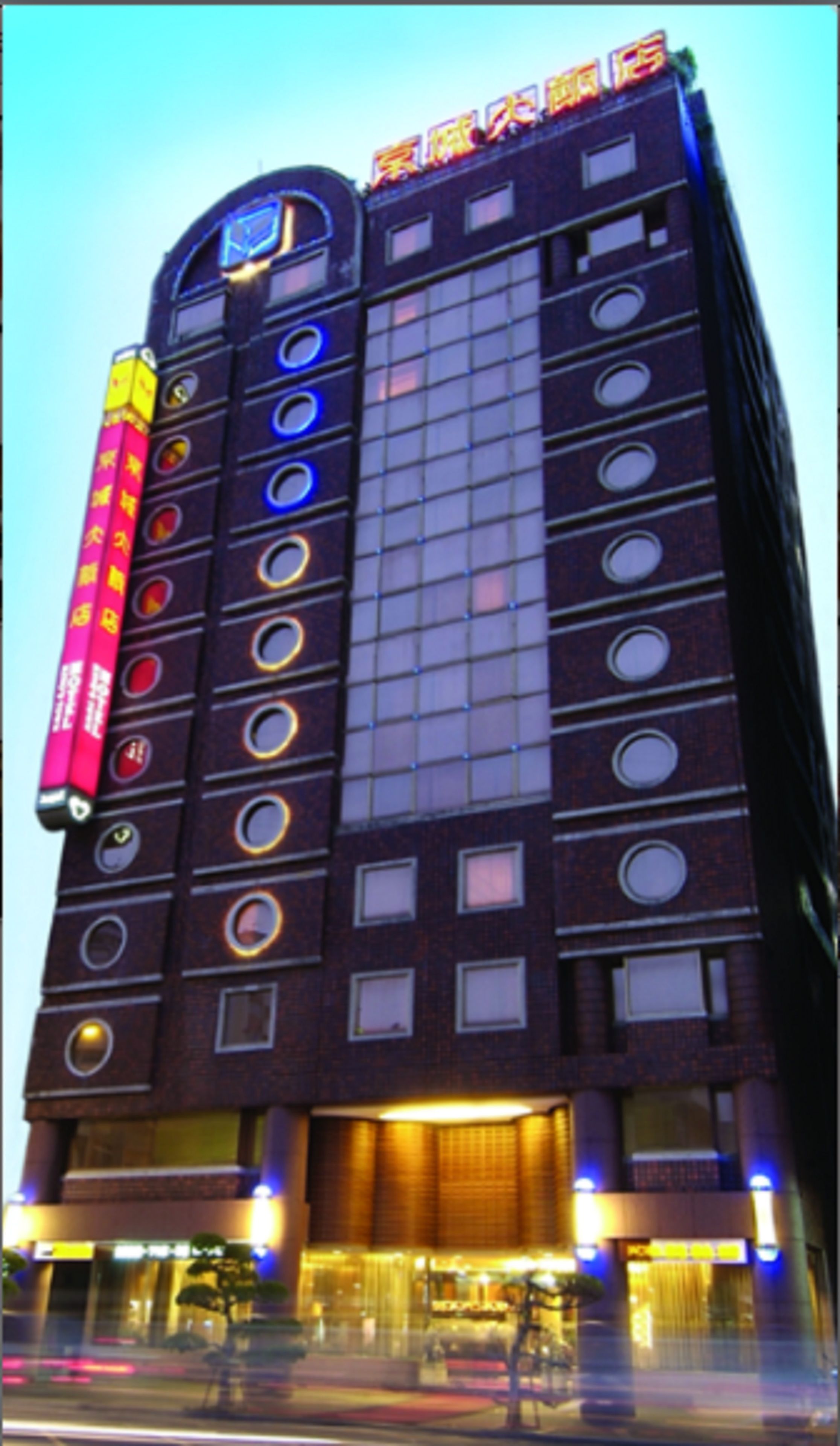 Een meerlaags hotel met een modern ontwerp, met een opvallend cirkelvormig patroon op de gevel en verlichte reclameborden.