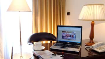 A hotel room desk with a laptop, a telephone, a lamp, a chair, a cup, and a newspaper.