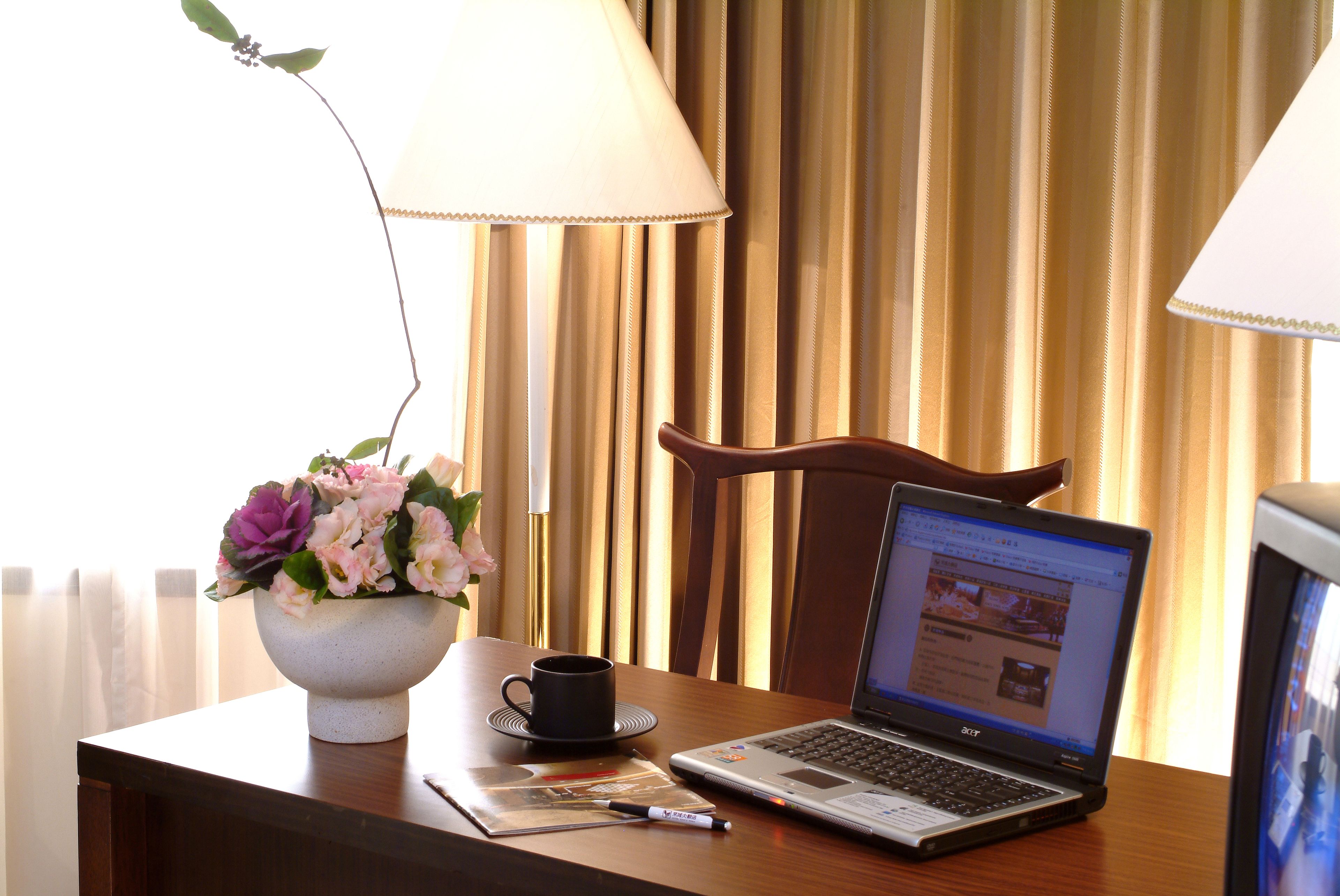 Una laptop sobre una mesa de madera con una taza, un bolígrafo y un florero.