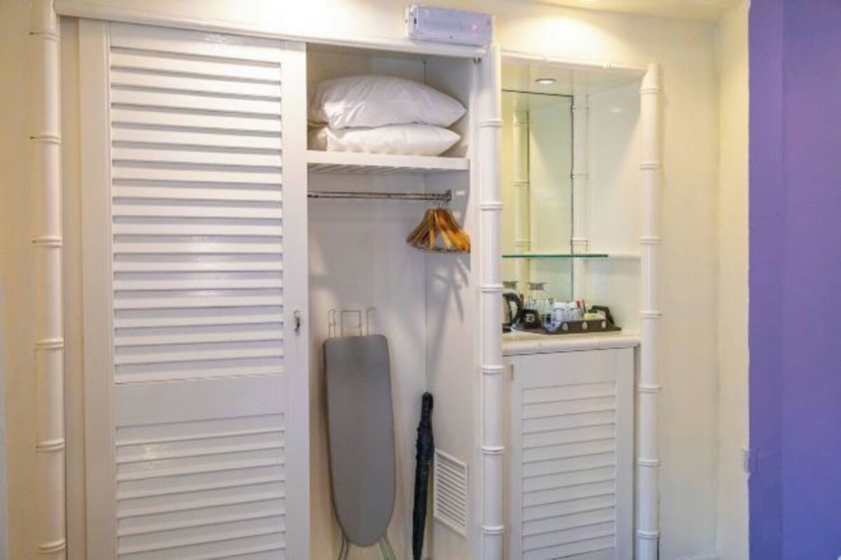 Une pièce avec un placard blanc, un miroir et une étagère sur laquelle se trouvent un coussin et un sac.