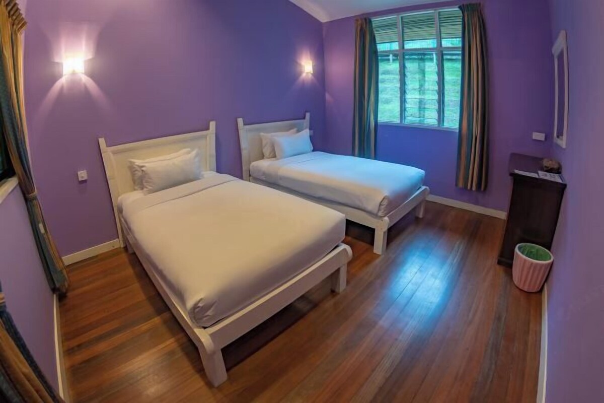 Une chambre avec deux lits, un plancher en bois, une fenêtre avec des rideaux et une poubelle.