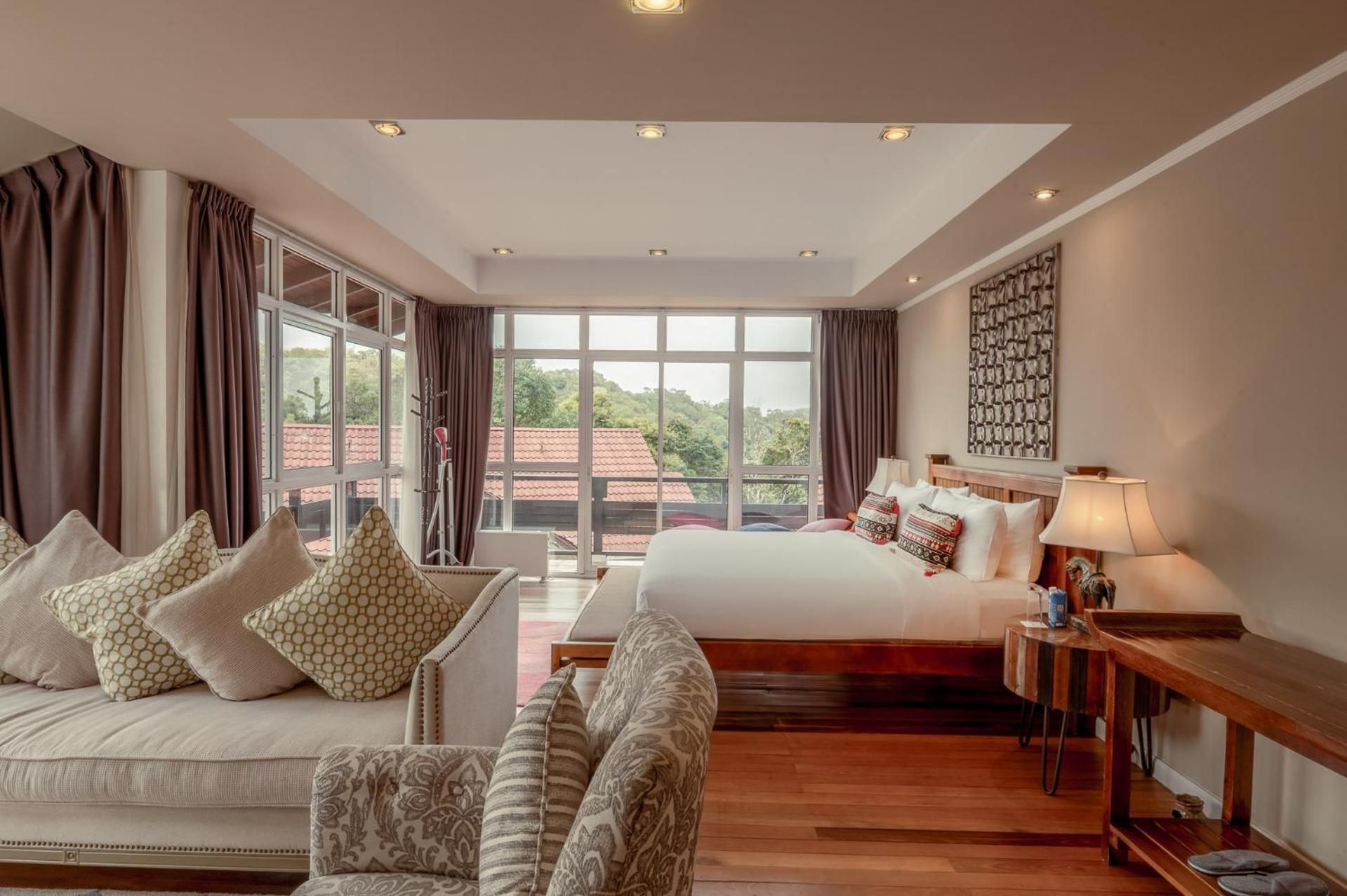 A hotel room with a large bed, a sofa, a desk with a lamp, and a view of the outdoors.
