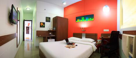 Una habitación de hotel con cama, escritorio con computadora portátil, silla, radiador y televisor en la pared.