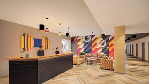 Un área de recepción moderna con un mostrador negro, ilustraciones de pared coloridas y asientos con estampado.