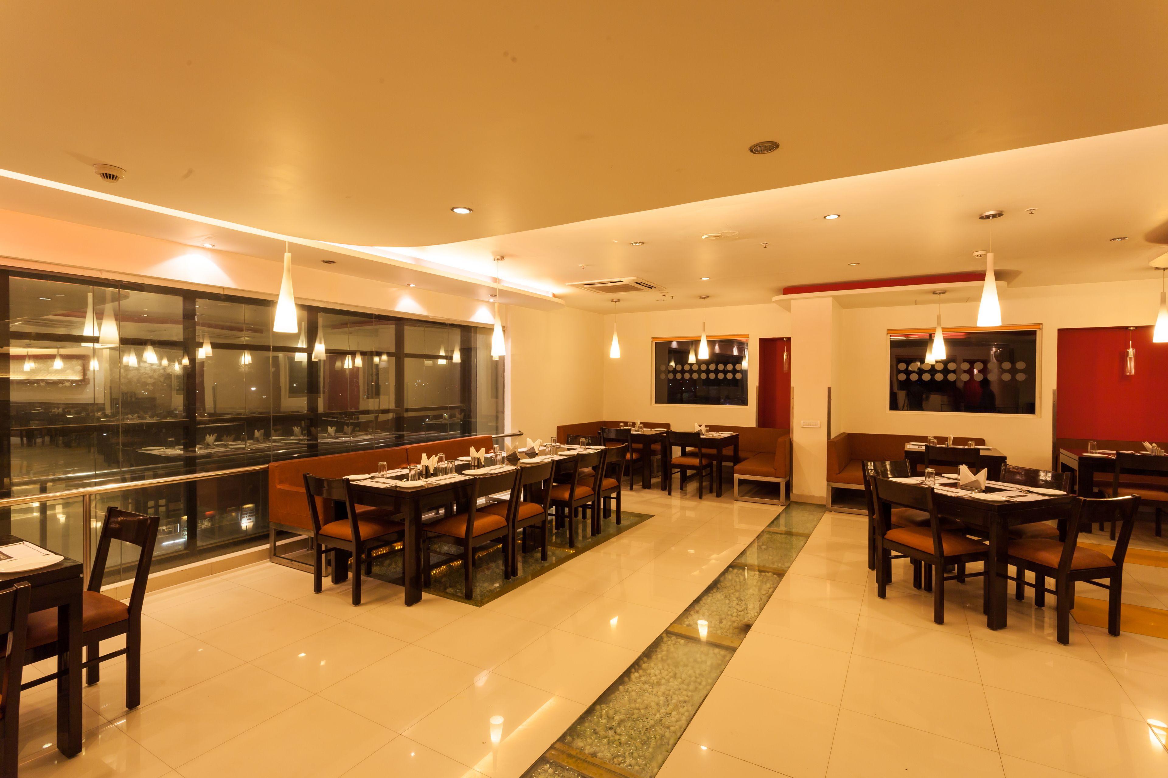 A spacious restaurant with multiple dining tables and chairs, large windows, and pendant lighting.