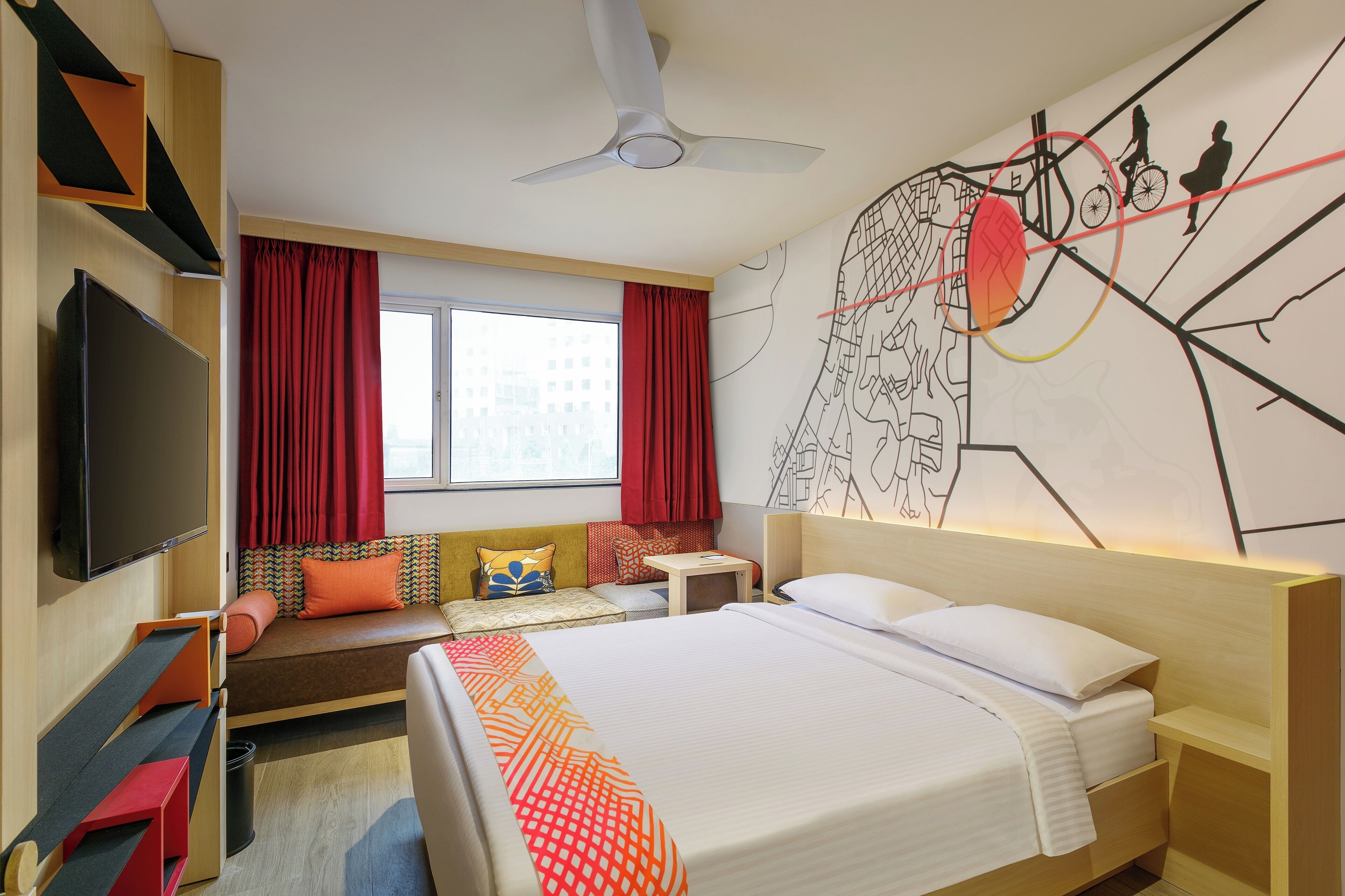 A hotel room with a bed, a TV, a desk, a chair, a sofa, and a window with curtains.