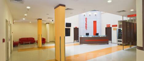 A modern hotel lobby with a reception desk, red seating area, and a vending machine.