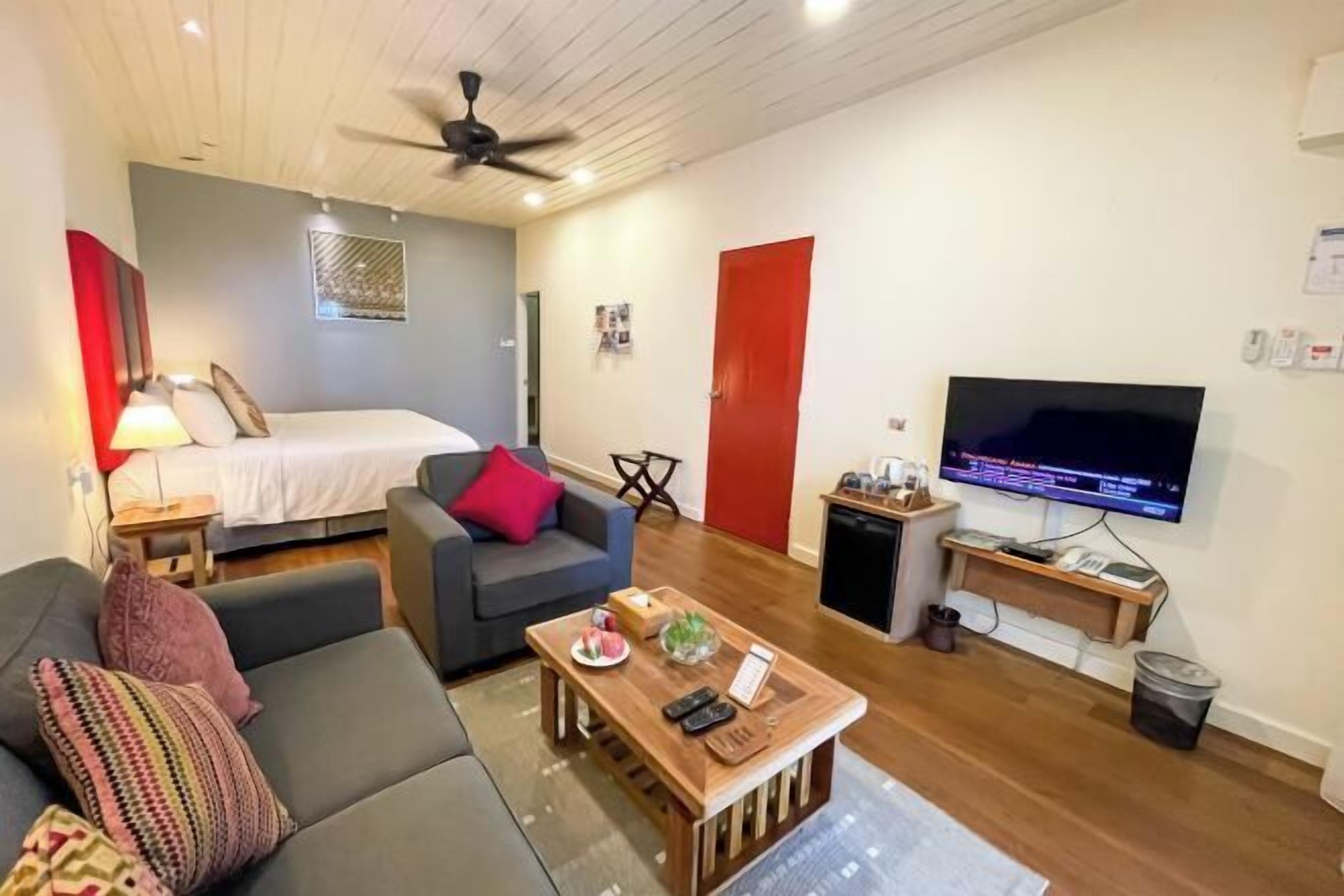 A compact living space with a bed, a sofa, a coffee table, a TV, and a ceiling fan.