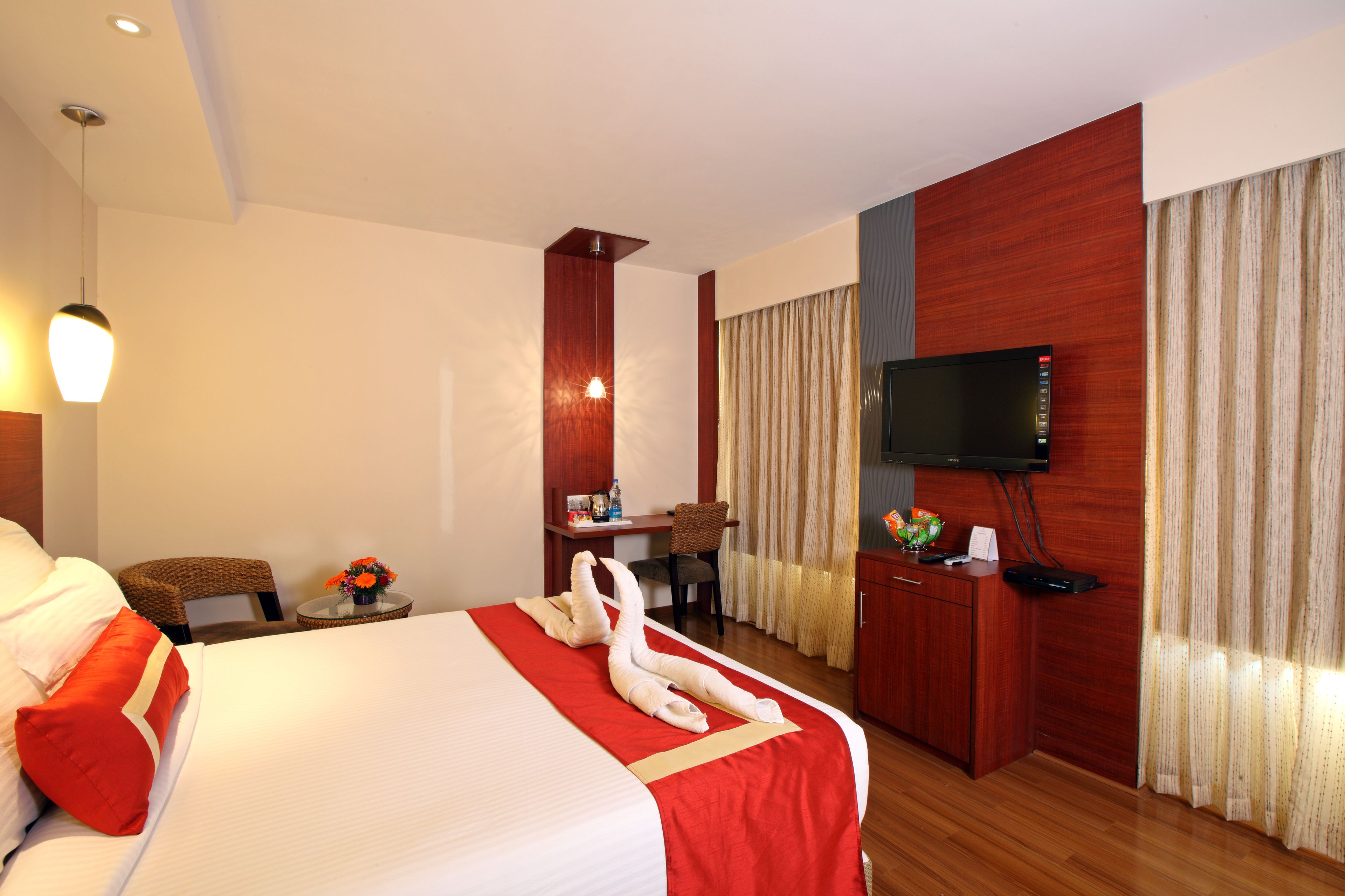 A hotel room with a large bed, a desk, a chair, a television, and a window with curtains.