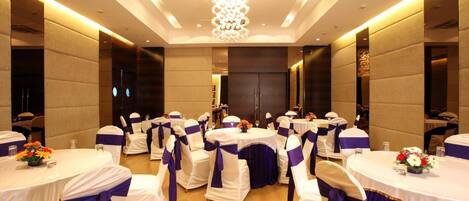 A banquet hall with round tables, white and purple tablecloths, and matching chair covers.