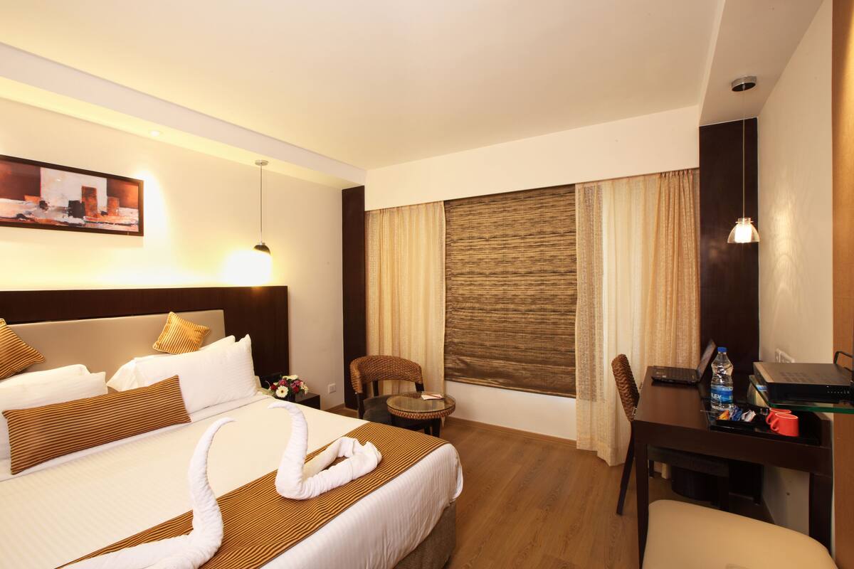 A hotel room with a large bed, a desk, a chair, a laptop, and a bottle of water.