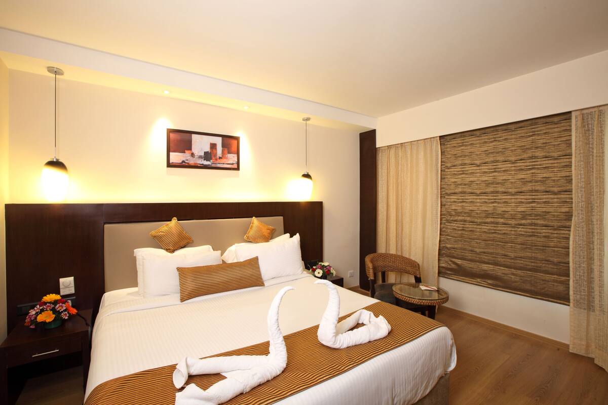 A hotel room with a large bed, two bedside tables, a small round table, and a large window with curtains.