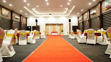 Un salón de conferencias con pasillo de alfombra roja, sillas blancas con lazos amarillos y un escenario decorado con flores.