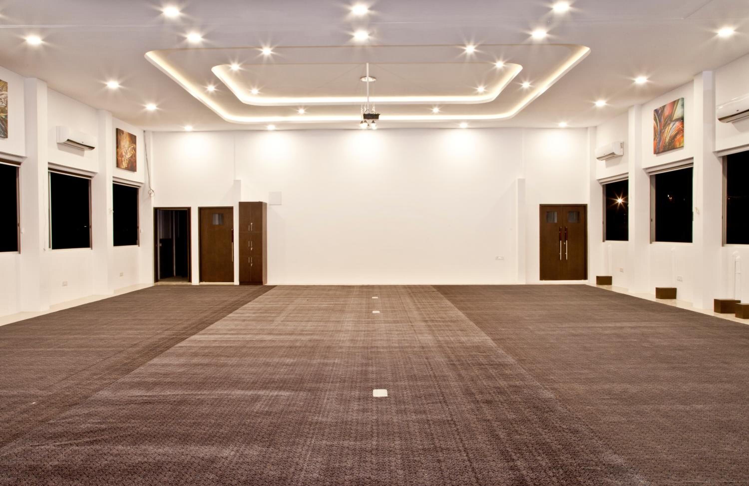 Una sala de conferències espaiosa i ben il·luminada, amb sòl de moqueta, parets blanques i diverses portes.
