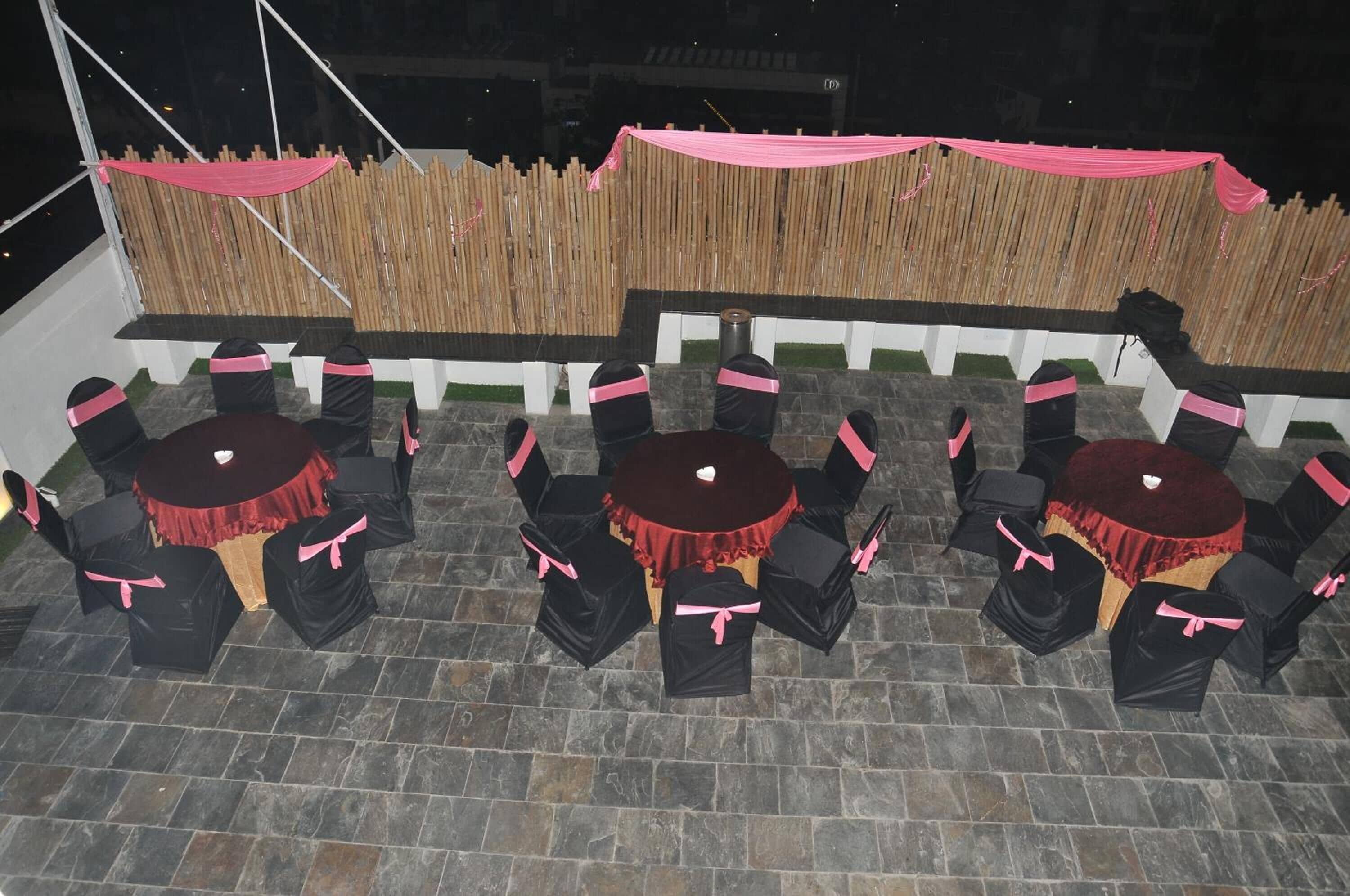 An outdoor patio area with round tables and chairs, bamboo screens, and a stone floor.