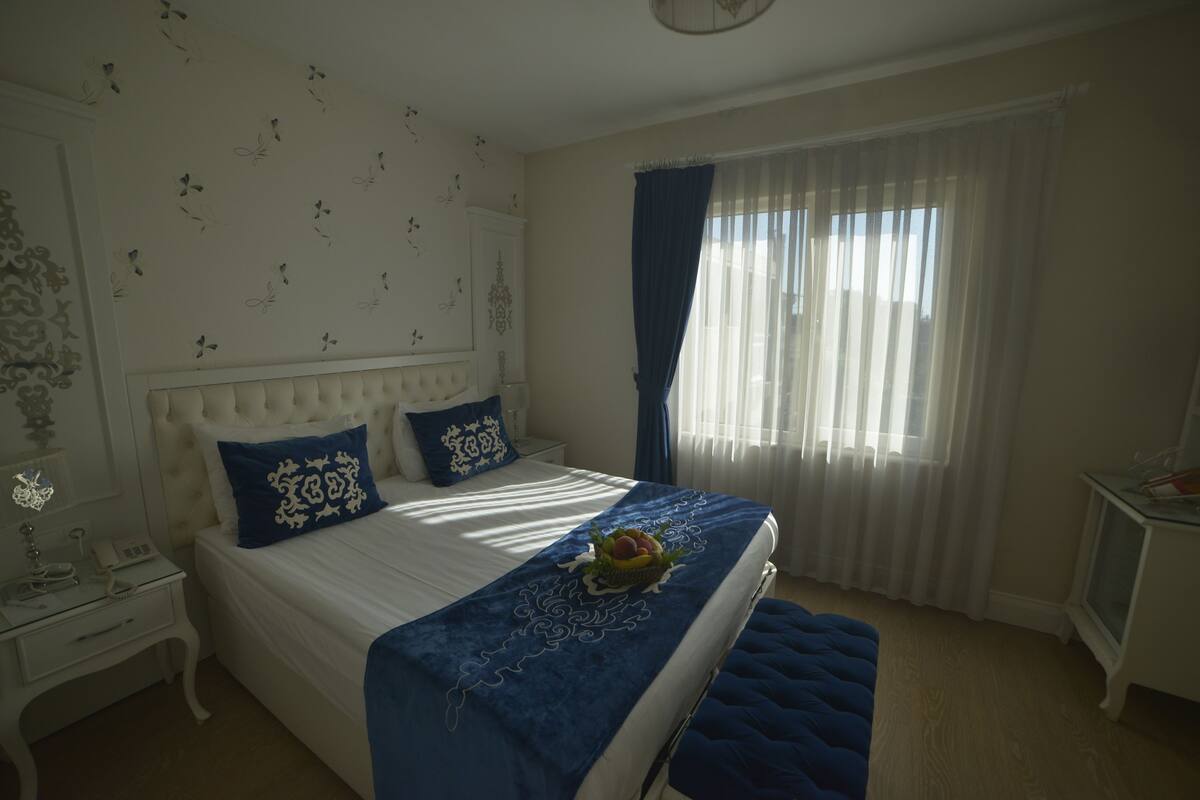 Une chambre à coucher comprenant un lit, une table de chevet, une commode, une fenêtre avec des rideaux et un mur décoré d’autocollants représentant des papillons.