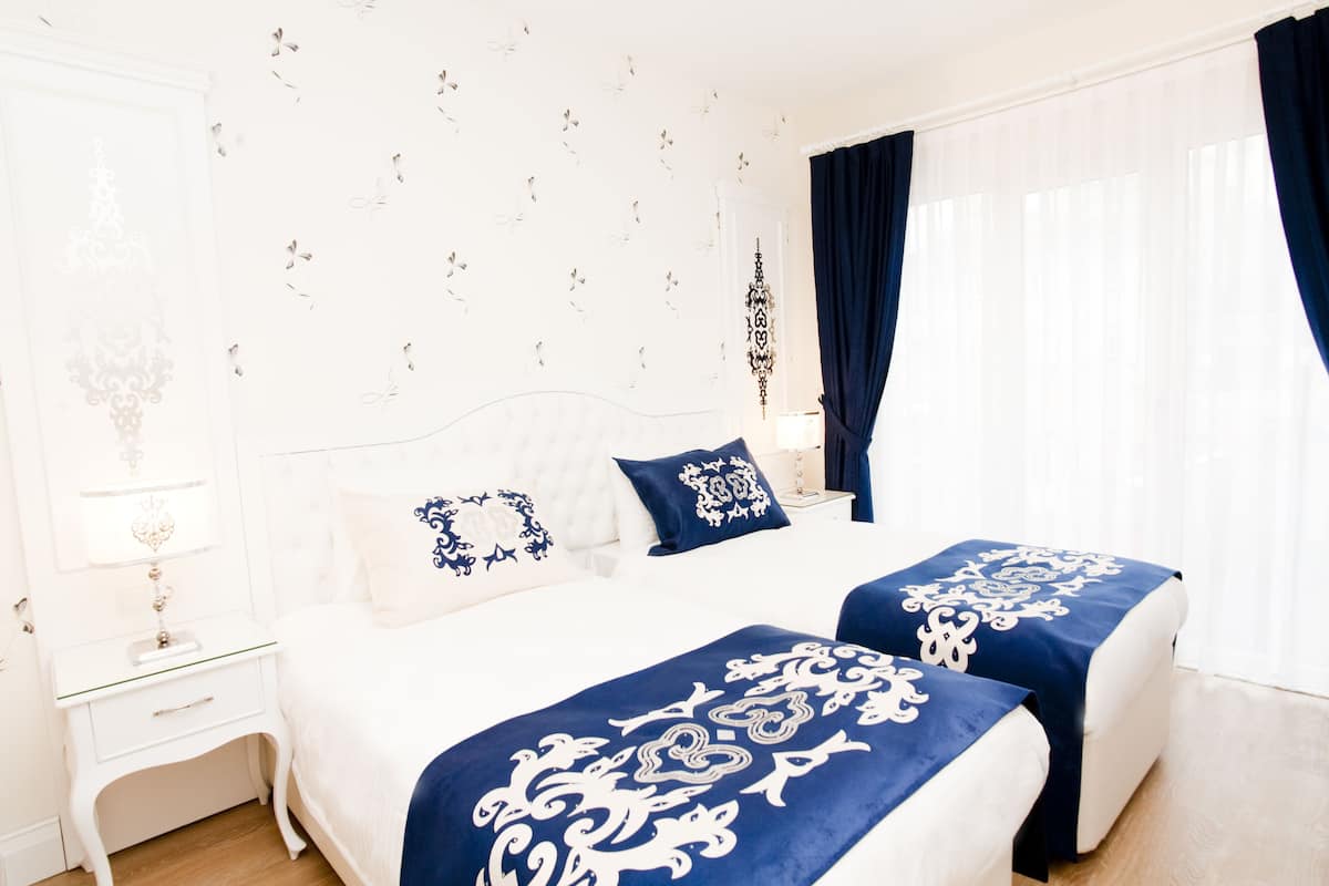 Une chambre d’hôtel avec un lit, deux tables de chevet, une commode et une fenêtre avec des rideaux.