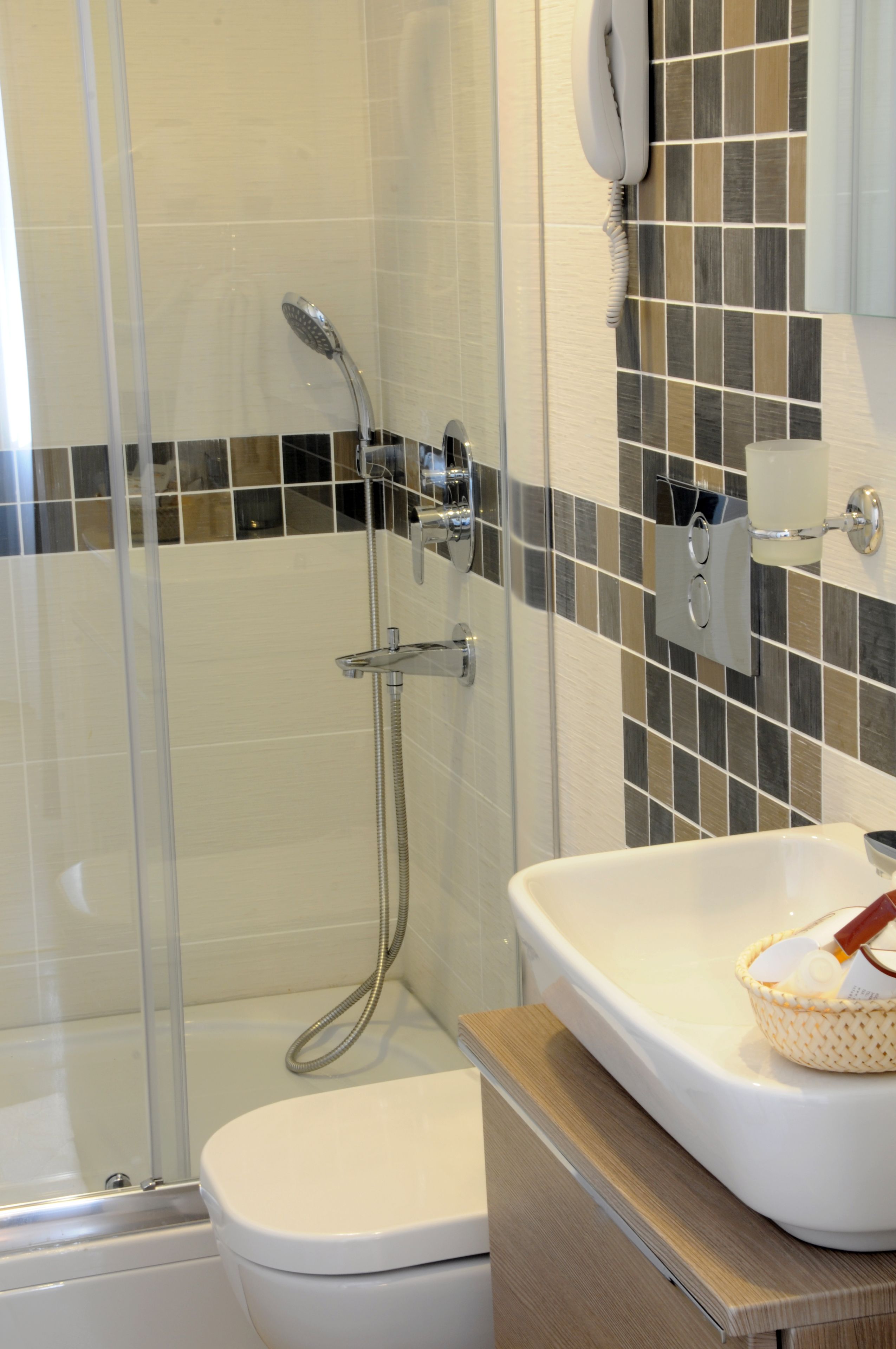 A modern bathroom with a glass-enclosed shower, a white toilet, and a sink with a basket of toiletries.