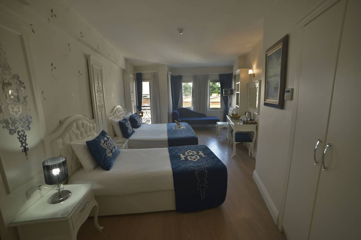 Une chambre d’hôtel avec deux lits, une table de chevet avec une lampe, un bureau avec une chaise et une armoire.